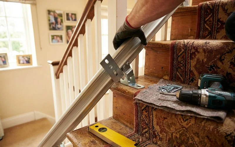 Close-up of stair lift rail brackets being securely mounted to wooden stair treads with professional tools